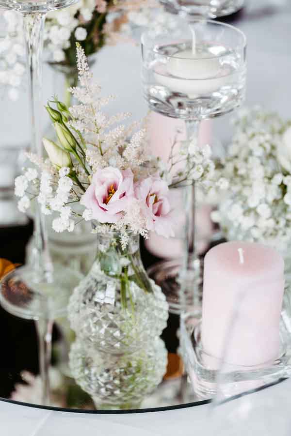 Blumenschmuck auf einem runden Spiegel auf dem Hochzeitstisch fotografiert.