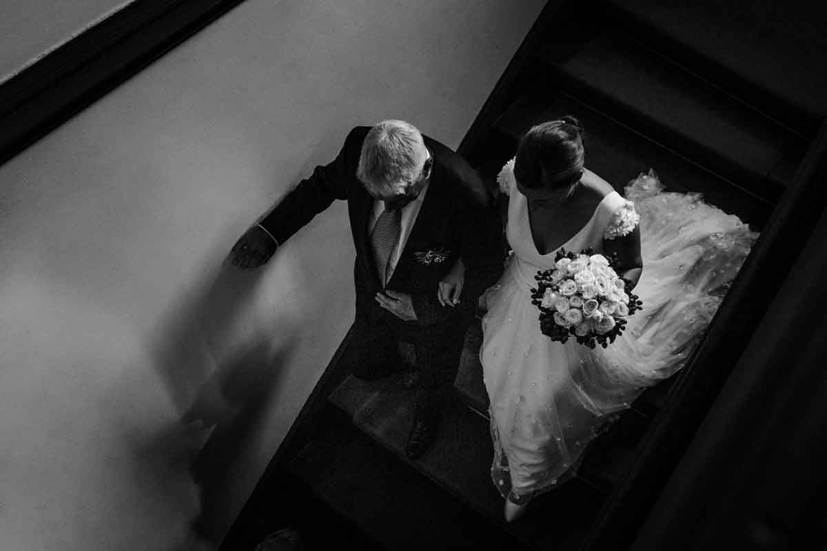 Brautvater begleitet die Braut zum Trauung. Sie gehen die Treppe herunter. Bild wurde von oben aufgenommen in schwarz-weiß.