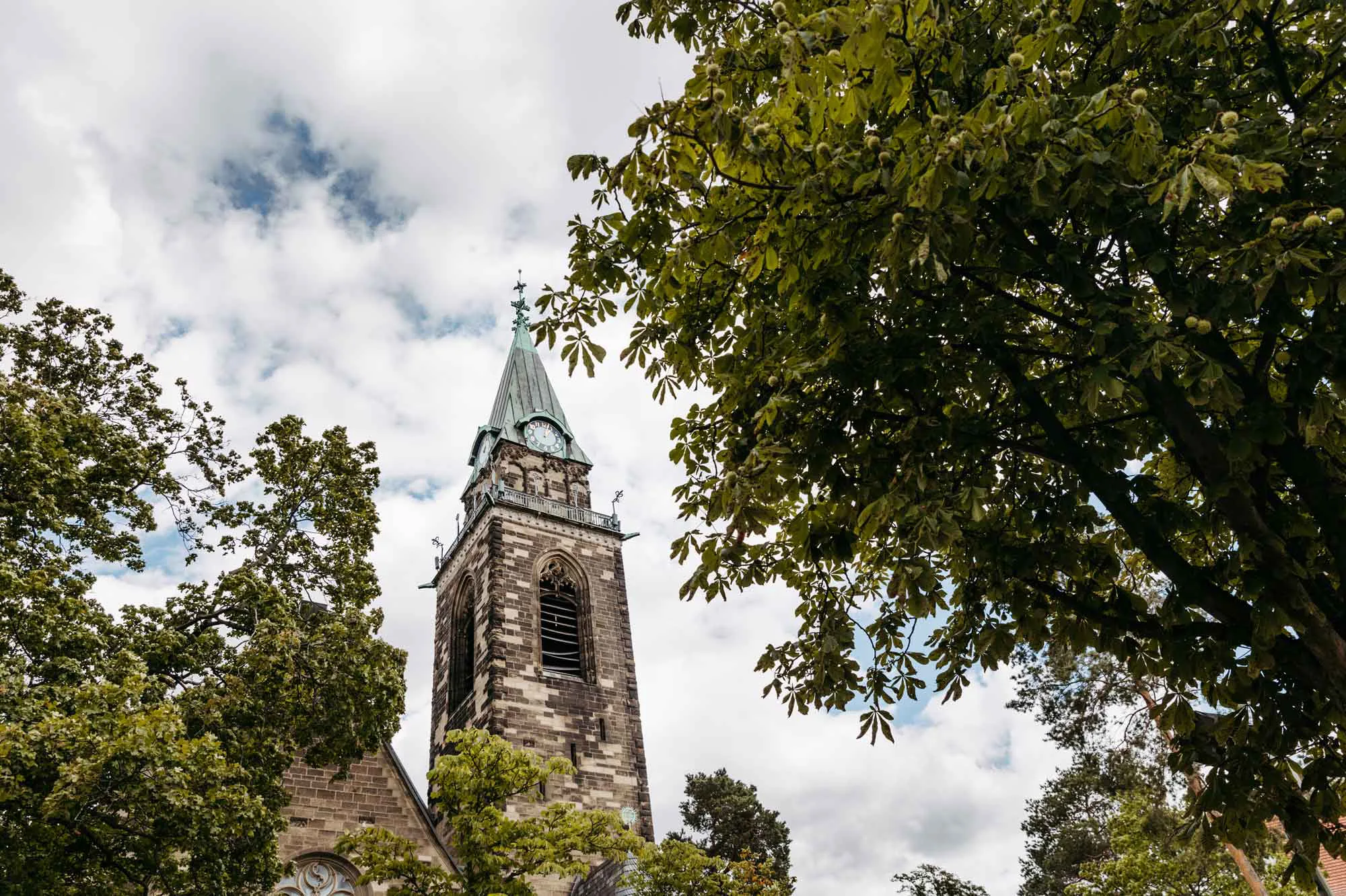 Außenaufnahme Grunewaldkirche. Mittig die Kirchturmspitze, rechts und links Bäume.