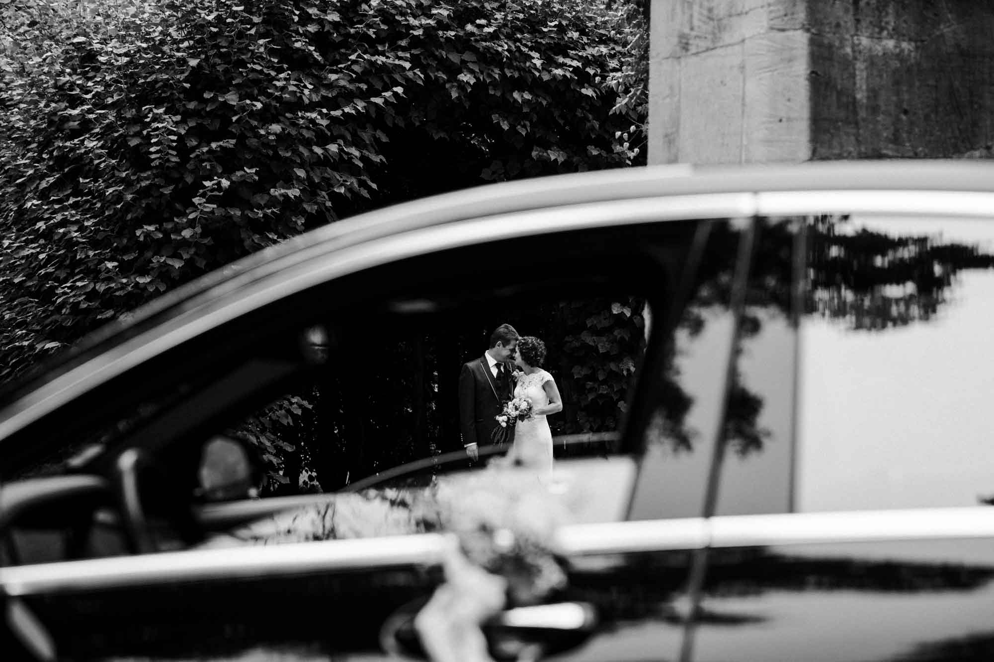 Verliebtes Brautpaar durch offene Autofensterscheibe fotografiert. Schwarz-weiß Aufnahme.