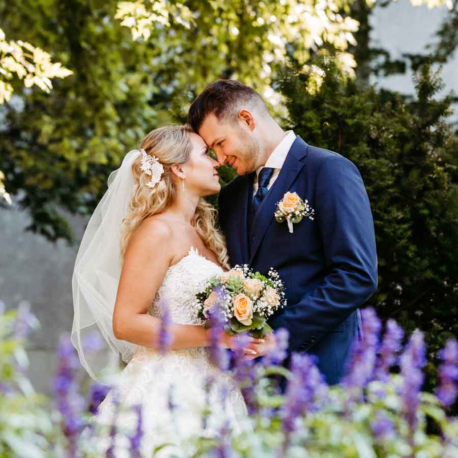 Brautpaar steht Stirn an Stirn. Im Vordergrund ist Lavendel. Im Hintergrund Bäume.