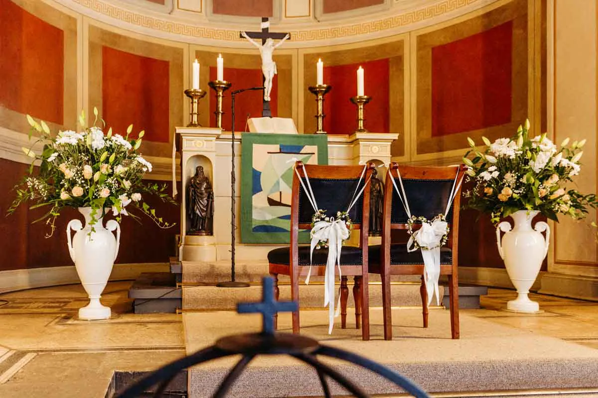 Nahaufnahme vom Traualtar der Kirche Nikolskoe am Wannsee. Traustühle in der Mitte vor dem Altar. Rechts und links größere Blumengestecke in einer weißen Vase.