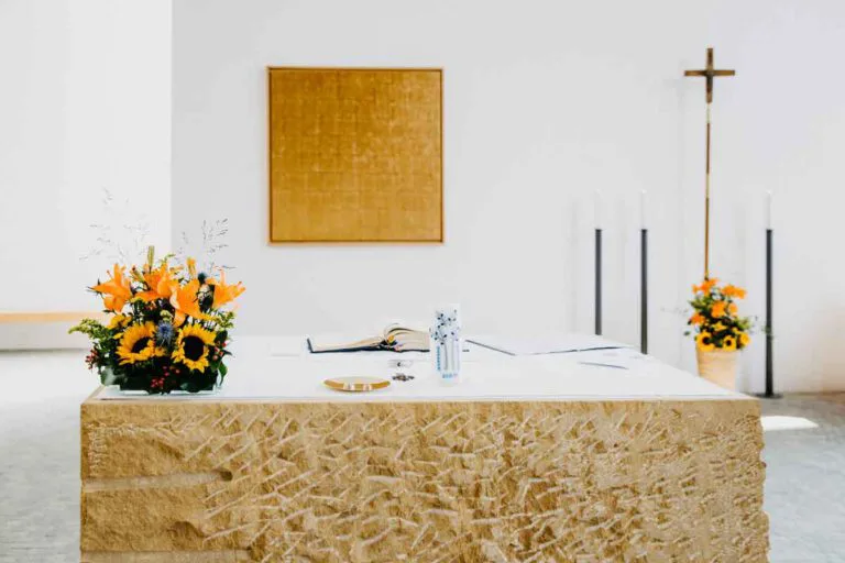 Frontansicht Altar der Sankt Canisius Kirche Charlottenburg mit einem Sonnenblumenstrauß links im Bild und mittig im Bild ist eine Taufkerze.
