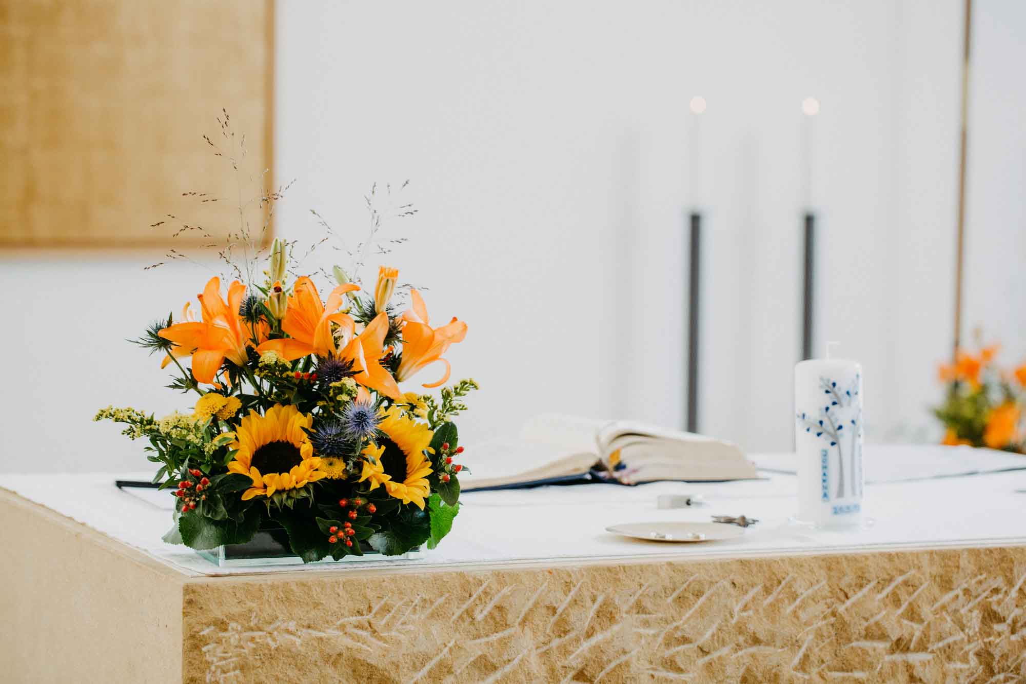 Sankt Canisius Kirche Altaransicht. Nahaufnahme. Links im Bild ein schöner Blumenstrauß mit Sonnenblumen. Rechts im Bild eine Taufkerze.