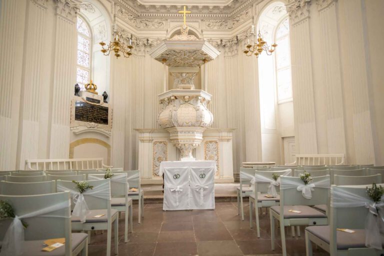 Schlosskirche Köpenick Innenaufnahme mit Blick auf den Altar. Rechts und links sind die Stühle für die Gäste mit Blumen und einem weißen Tuch geschmückt.