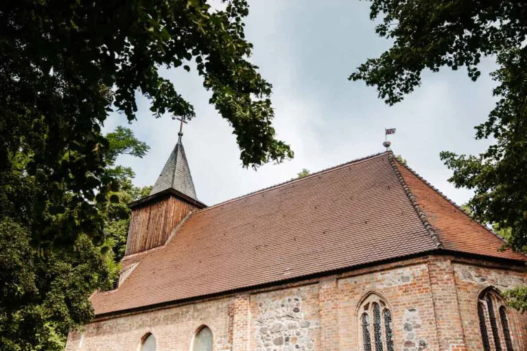 Detailaufnahme von der St. Annen Kirche in Berlin Dahlem. Bäume stehen im Vordergrund und dienen als Rahmen.
