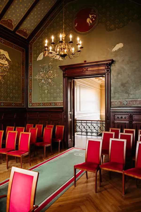 Standesamt Neukölln Trauzimmer Kapelle mit roter Bestuhlung und einem Kronleuchter sowie wunderschöner Wandbemahlung.