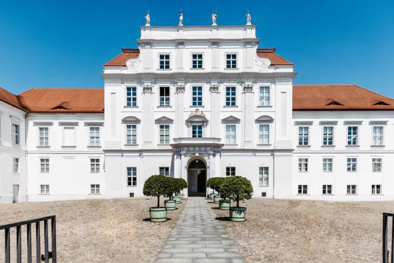 Frontansicht Schloss Oranienburg. Zum Eingang stehen rechts und links kleine Bäume in Pflanzkästen.