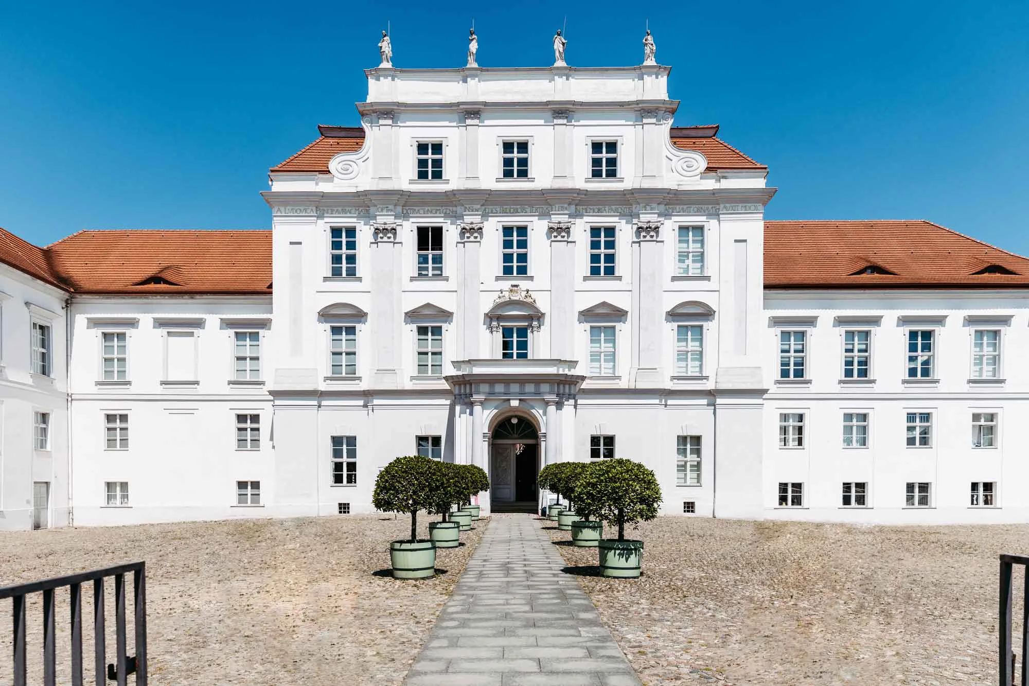 Frontansicht Schloss Oranienburg. Zum Eingang stehen rechts und links kleine Bäume in Pflanzkästen.