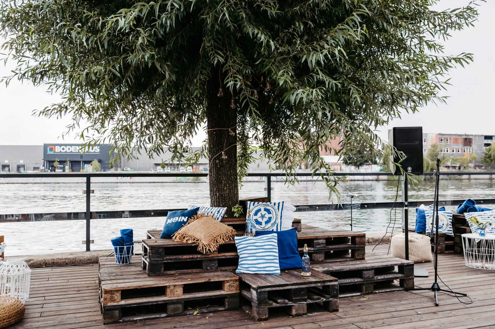 Chillarea mit Kissen auf Paletten rund um einen Baum mit Blick auf die Spree.